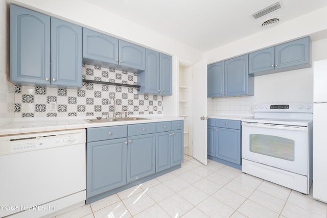 kitchen featuring light tile patterned floors, backsplash, a sink, blue cabinets, and white appliances