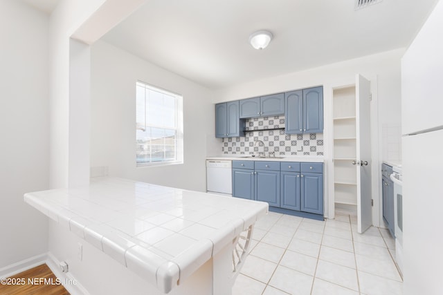 kitchen featuring blue cabinetry, decorative backsplash, white dishwasher, a sink, and a peninsula