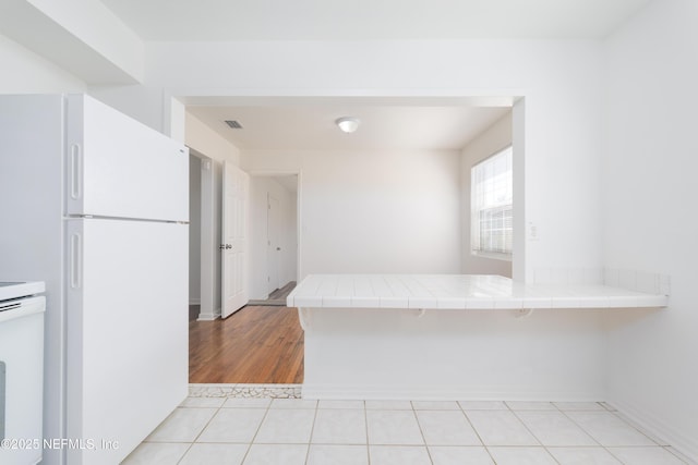 kitchen with tile counters, freestanding refrigerator, visible vents, and a peninsula