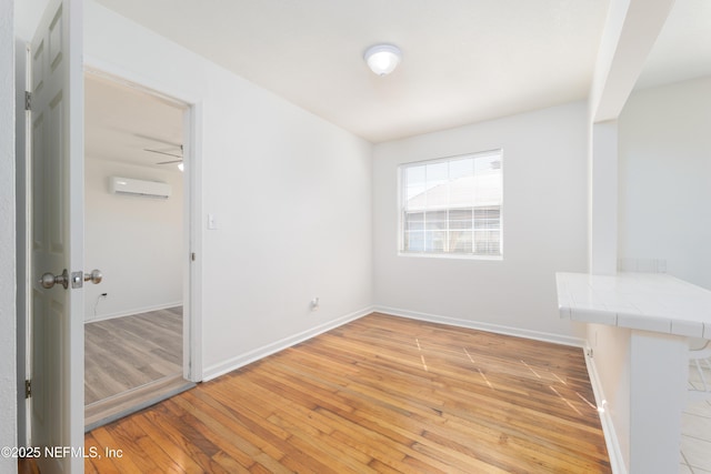 unfurnished room featuring baseboards, a wall unit AC, and light wood finished floors