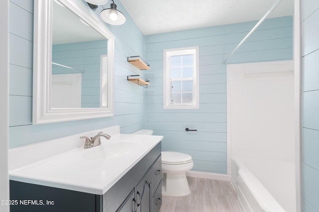 full bathroom featuring a textured ceiling, toilet, wood walls, wood finished floors, and vanity