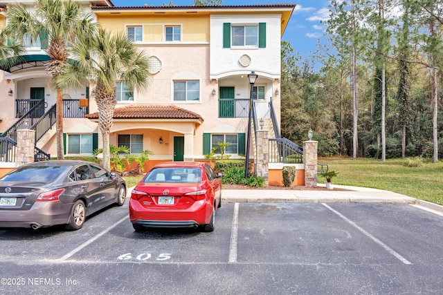 view of front of house with a tiled roof, uncovered parking, stairway, and stucco siding