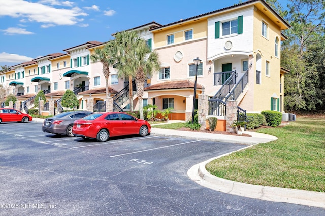 view of property with uncovered parking, a residential view, stairs, and central AC unit