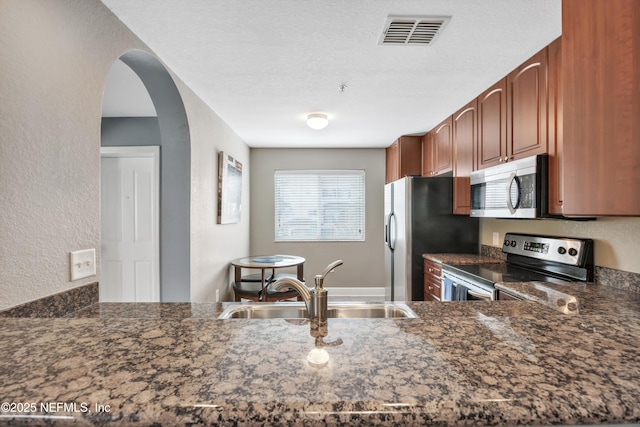 kitchen featuring arched walkways, visible vents, dark stone counters, stainless steel appliances, and a sink