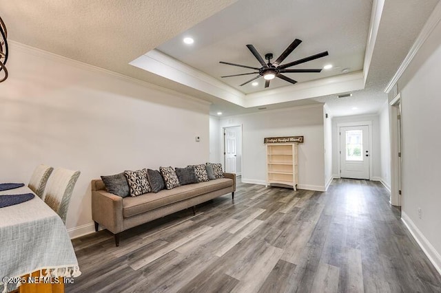 living area with a raised ceiling, crown molding, baseboards, and wood finished floors