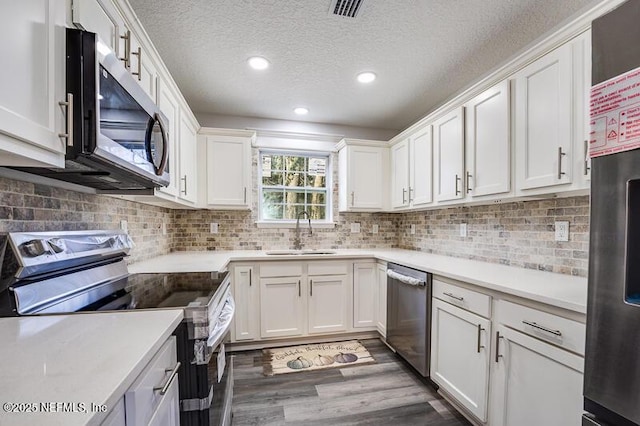 kitchen featuring tasteful backsplash, white cabinets, appliances with stainless steel finishes, wood finished floors, and a sink