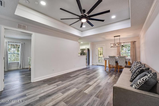 living room featuring a tray ceiling, wood finished floors, visible vents, and crown molding