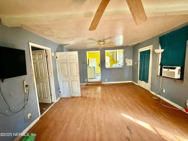 unfurnished bedroom with an AC wall unit, baseboards, and wood finished floors