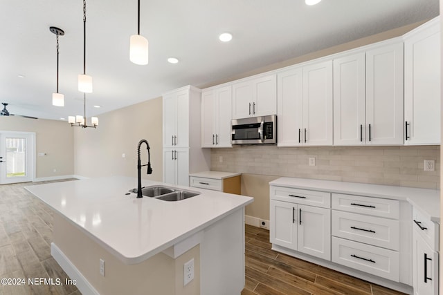 kitchen with wood finish floors, pendant lighting, tasteful backsplash, stainless steel microwave, and a sink