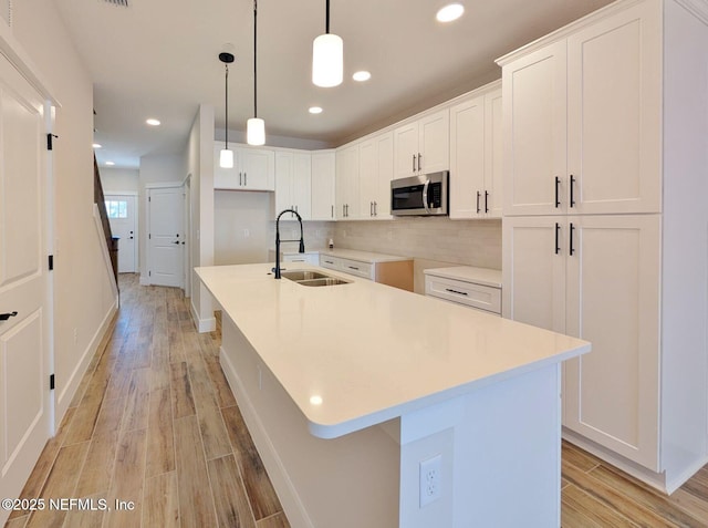 kitchen featuring tasteful backsplash, stainless steel microwave, light wood-style floors, white cabinets, and a sink