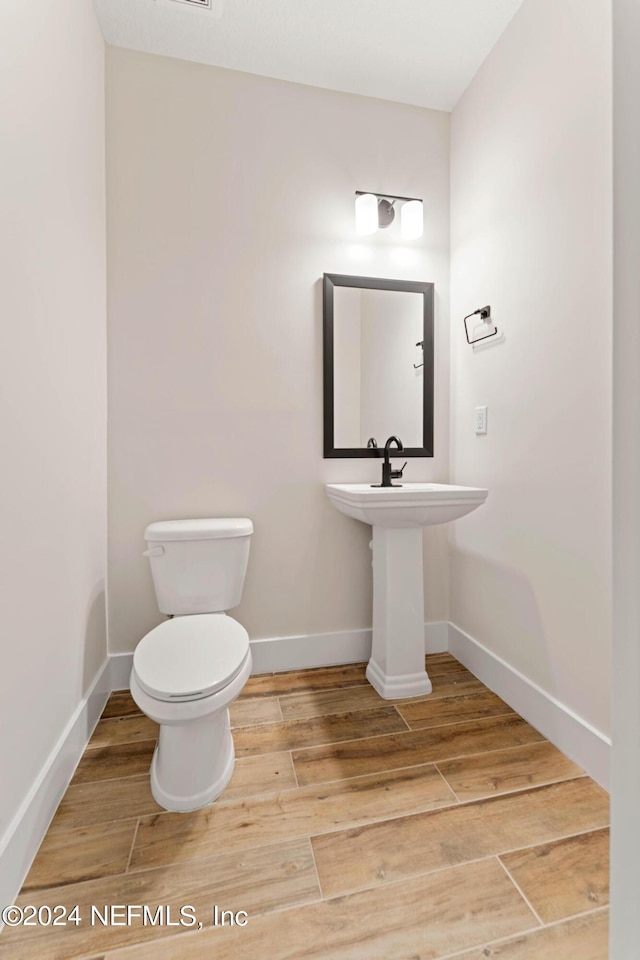 half bath featuring toilet, baseboards, and wood finished floors