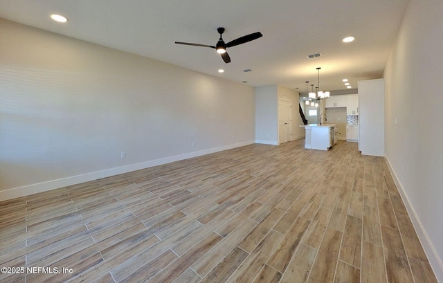 unfurnished living room with ceiling fan with notable chandelier, light wood-type flooring, visible vents, and baseboards