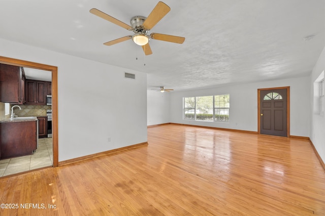 unfurnished living room featuring light wood-type flooring, visible vents, a sink, and baseboards