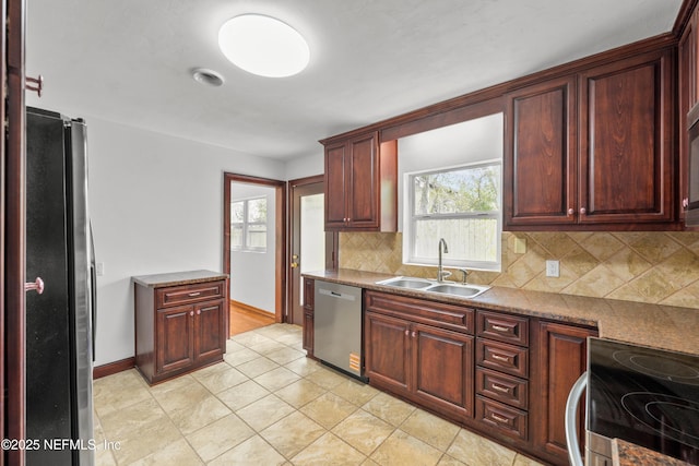 kitchen featuring light tile patterned floors, stainless steel appliances, a sink, baseboards, and tasteful backsplash