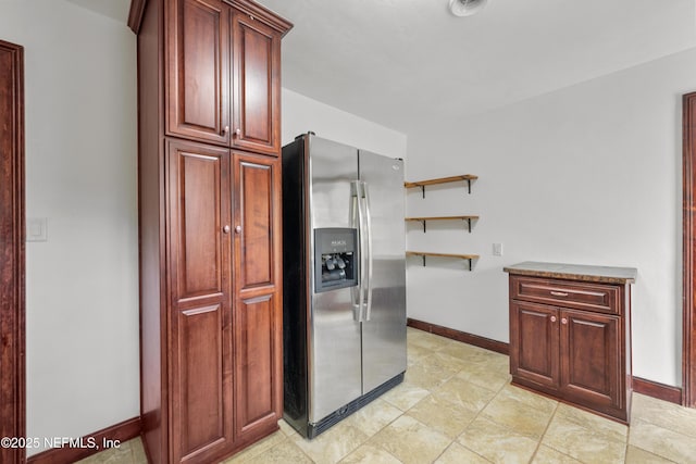 kitchen featuring stone counters, stainless steel refrigerator with ice dispenser, open shelves, dark brown cabinets, and baseboards