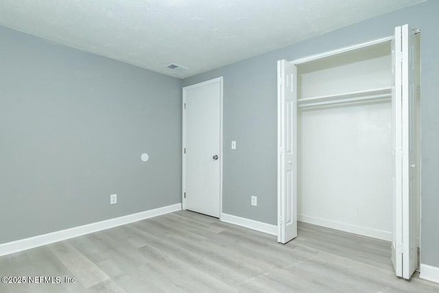 unfurnished bedroom featuring a textured ceiling, visible vents, baseboards, a closet, and light wood-type flooring