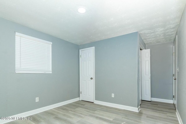 unfurnished bedroom featuring light wood-style floors, baseboards, and a textured ceiling