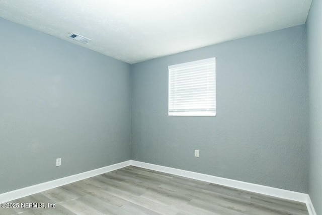 spare room with wood finished floors, visible vents, and baseboards