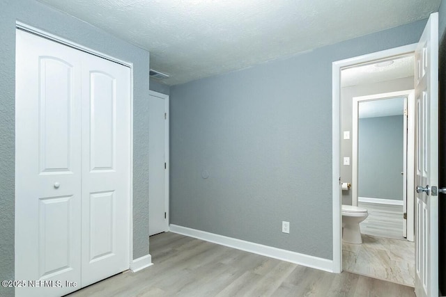 bedroom with connected bathroom, wood finished floors, visible vents, baseboards, and a closet