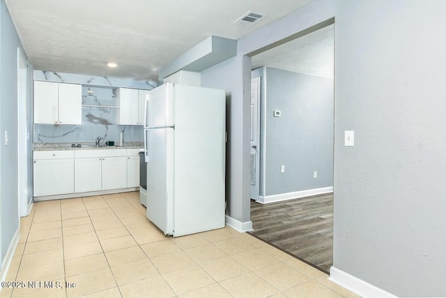 kitchen featuring light countertops, visible vents, freestanding refrigerator, white cabinetry, and a sink