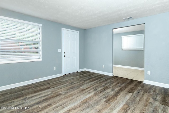 unfurnished room with visible vents, a textured ceiling, baseboards, and wood finished floors