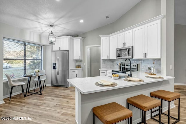 kitchen featuring a breakfast bar area, tasteful backsplash, light countertops, appliances with stainless steel finishes, and a peninsula