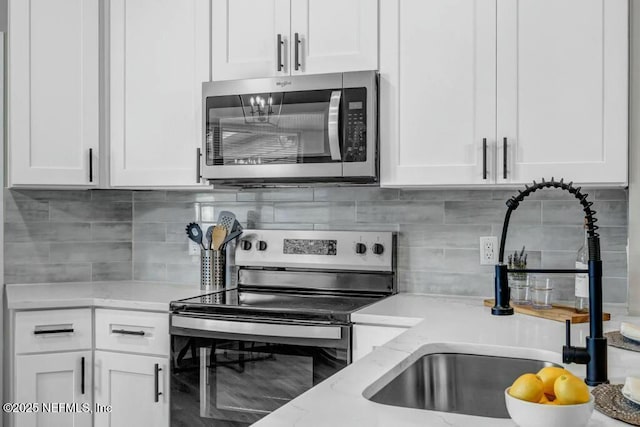 kitchen with backsplash, white cabinetry, stainless steel appliances, and a sink