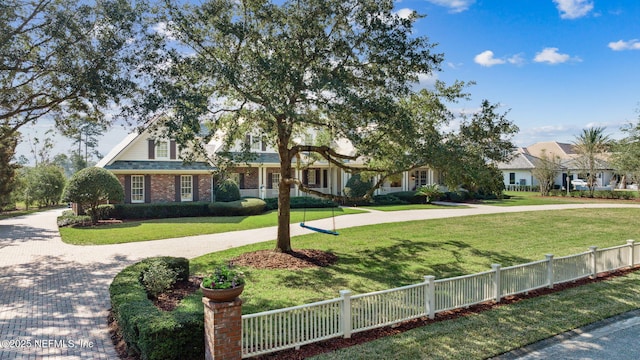 view of front of house with a front lawn, a fenced front yard, curved driveway, and brick siding