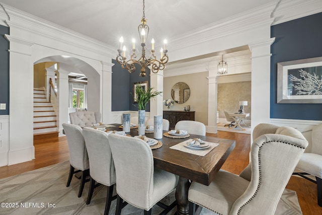 dining space with arched walkways, ornamental molding, wainscoting, wood finished floors, and ornate columns