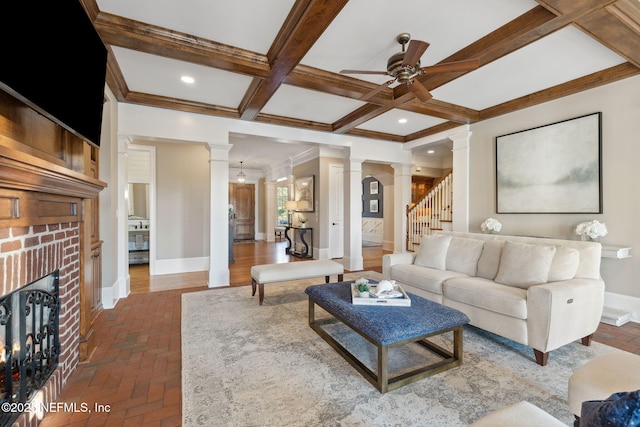 living area featuring ornate columns, a brick fireplace, baseboards, and a ceiling fan