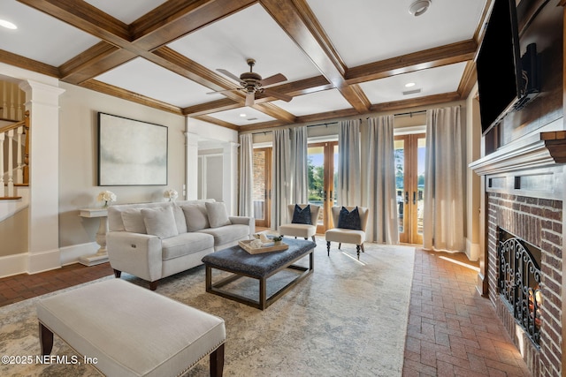 living room featuring a brick fireplace, ornate columns, beamed ceiling, and baseboards