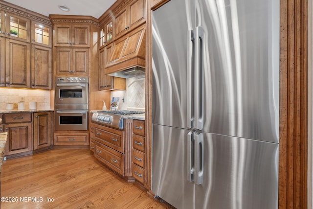 kitchen with light stone counters, appliances with stainless steel finishes, brown cabinetry, and light wood-style flooring