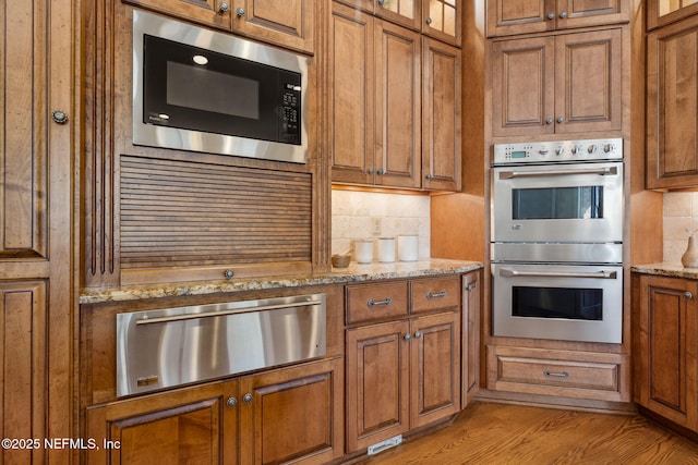 kitchen featuring stainless steel double oven, backsplash, built in microwave, a warming drawer, and brown cabinetry