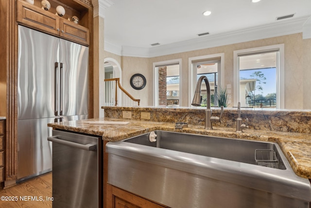 kitchen with ornamental molding, appliances with stainless steel finishes, a sink, and brown cabinets