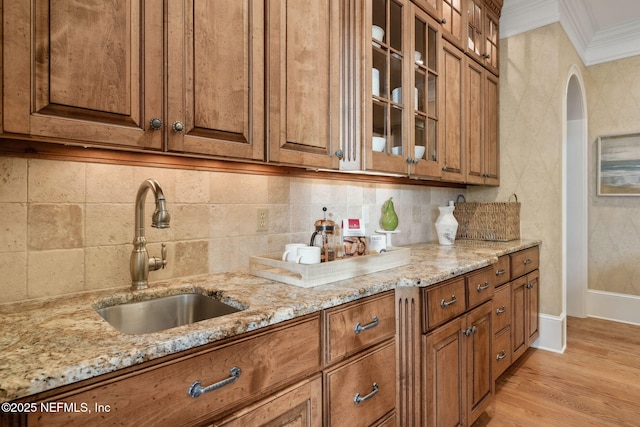 kitchen with a sink, ornamental molding, brown cabinetry, and light stone counters