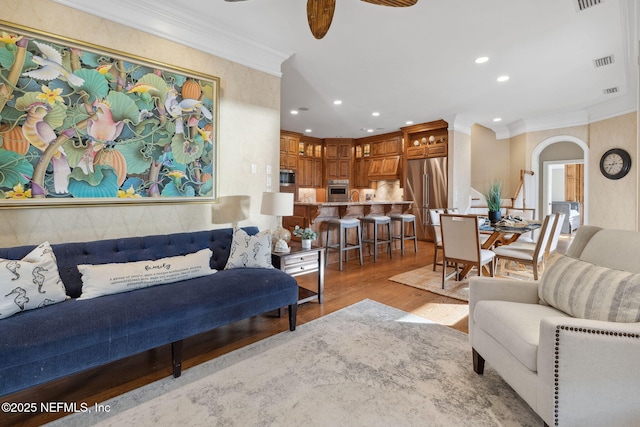 living room featuring ceiling fan, recessed lighting, visible vents, light wood finished floors, and crown molding