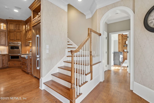 stairway with ornamental molding, arched walkways, baseboards, and wood finished floors