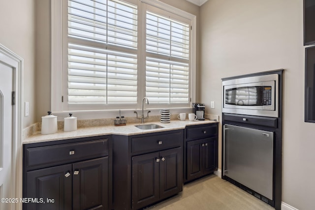 kitchen with light carpet, stainless steel microwave, light stone counters, and a sink