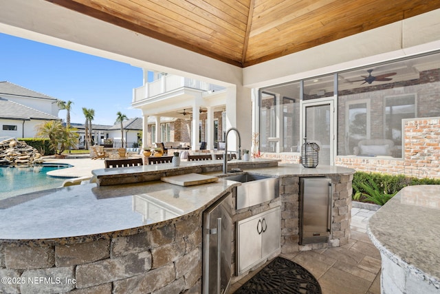 view of patio with an outdoor pool, an outdoor kitchen, a balcony, ceiling fan, and a sink