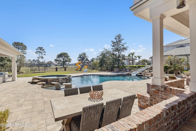 view of swimming pool featuring a patio, fence, a water slide, a pool with connected hot tub, and a playground