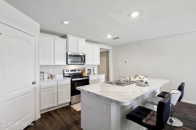 kitchen with dark wood-style flooring, visible vents, appliances with stainless steel finishes, a kitchen island with sink, and a sink