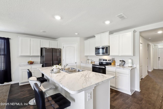 kitchen with a kitchen island with sink, stainless steel appliances, a sink, visible vents, and dark wood-style floors