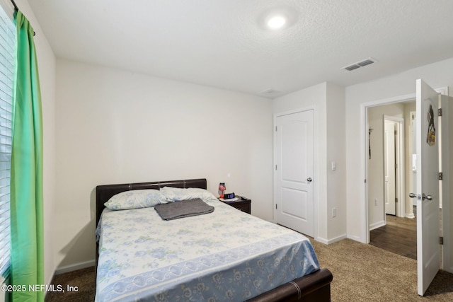 carpeted bedroom featuring a textured ceiling, visible vents, and baseboards