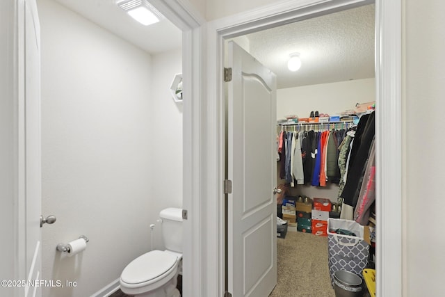 bathroom featuring a textured ceiling, a spacious closet, toilet, and baseboards