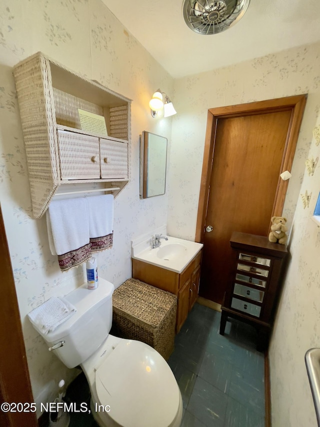 half bathroom with tile patterned floors, vanity, toilet, and wallpapered walls