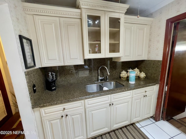 kitchen with a sink, ornamental molding, dark stone countertops, glass insert cabinets, and wallpapered walls