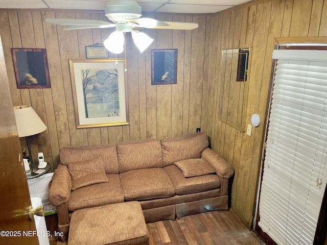 living room with ceiling fan, wood walls, and wood finished floors