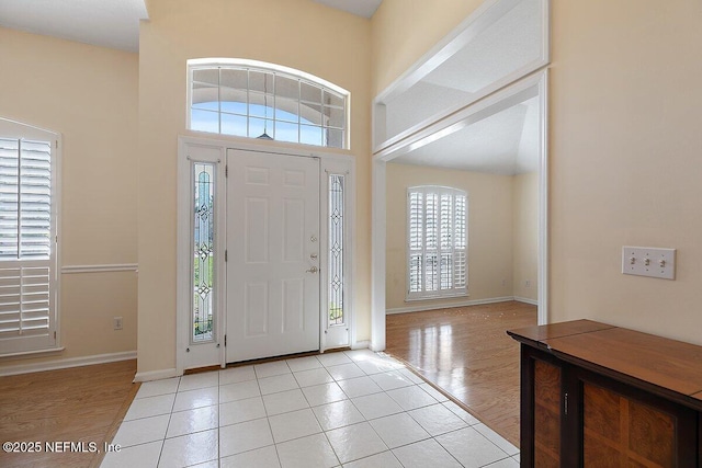 entrance foyer with baseboards, light wood-style floors, and a towering ceiling