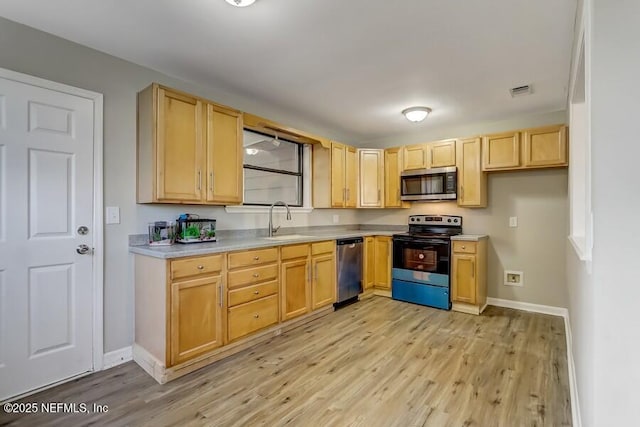 kitchen featuring light wood-style floors, appliances with stainless steel finishes, a sink, and light brown cabinetry