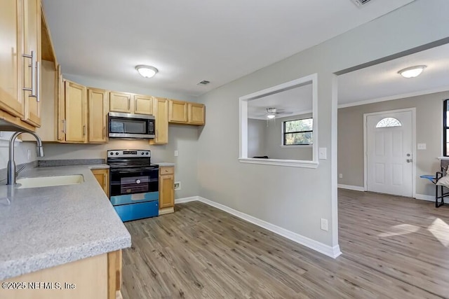 kitchen with electric range oven, stainless steel microwave, light countertops, light brown cabinets, and a sink